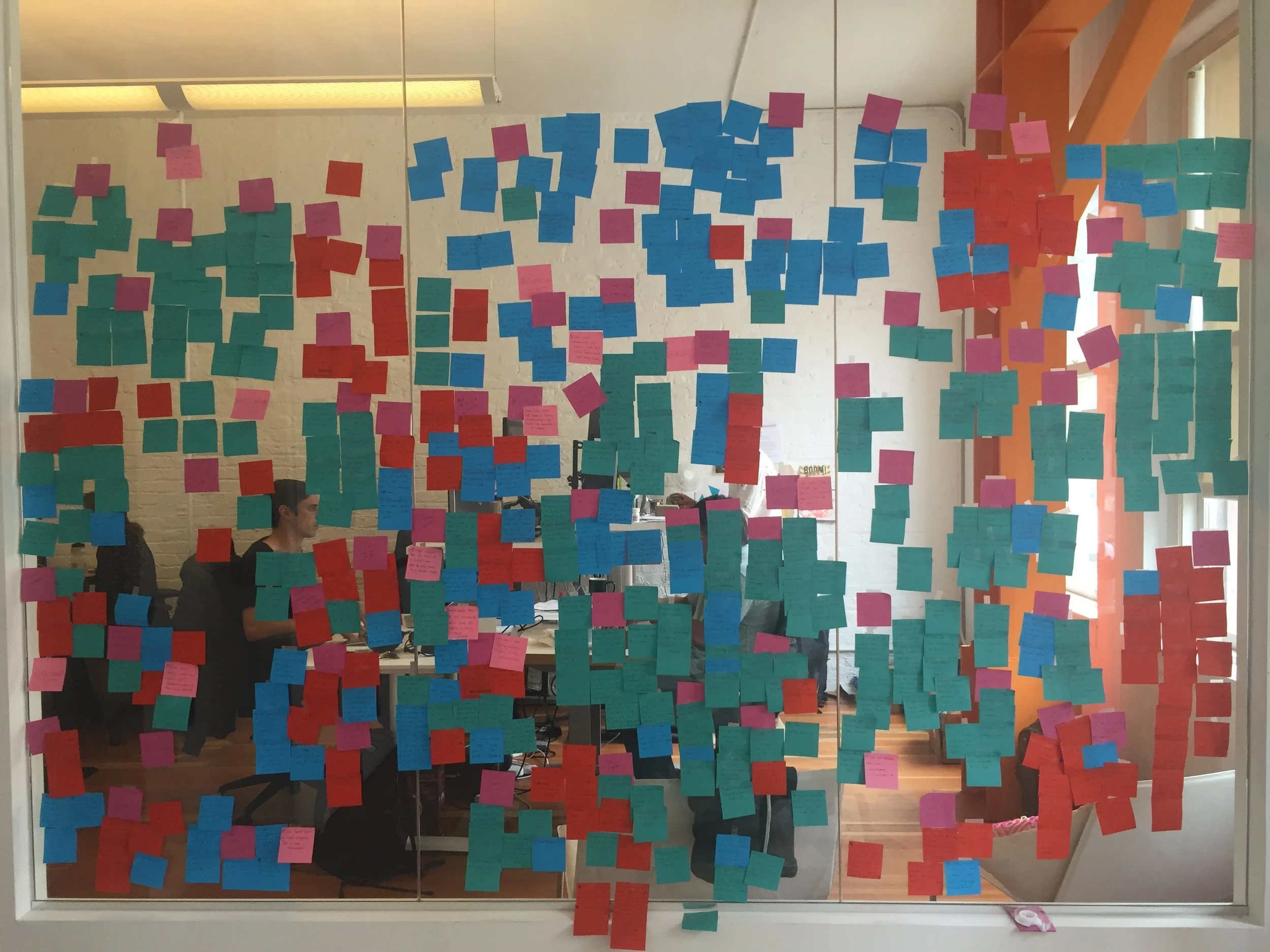 A glass wall covered in colorful Post-It notes organized in clusters during interview analysis.